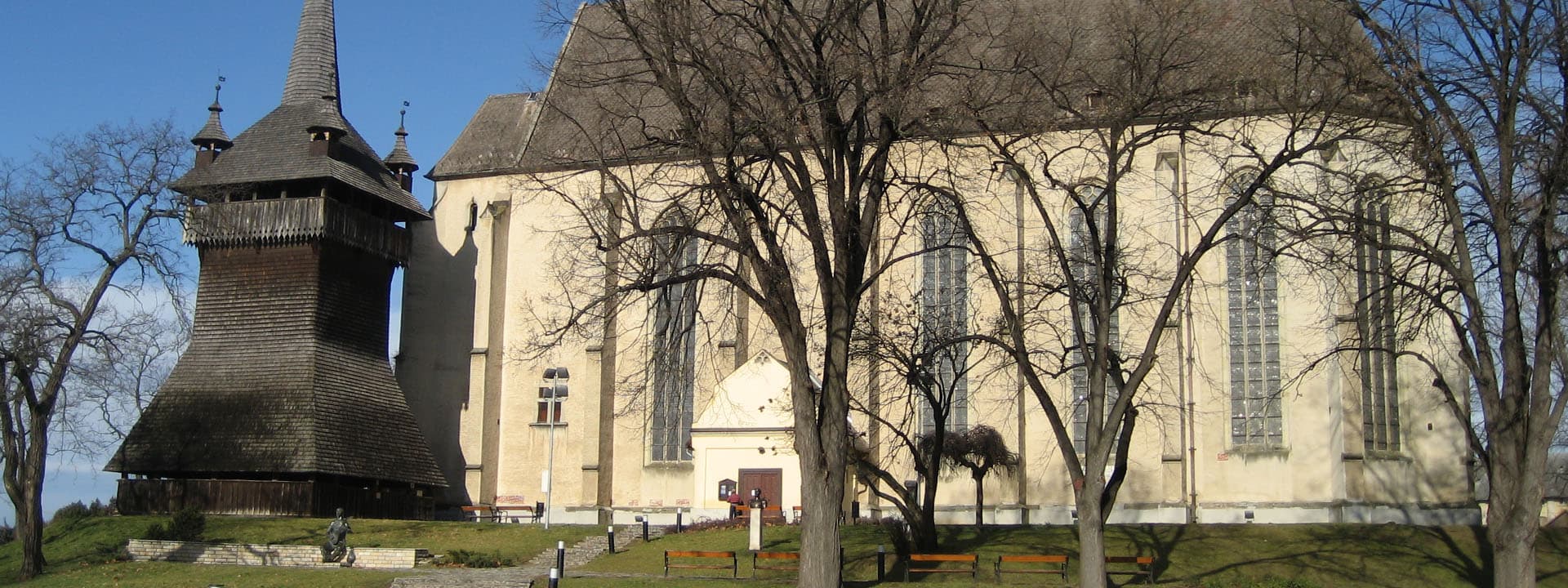 Nyírbátor városképe történelmi templommal és fa harangtoronnyal.